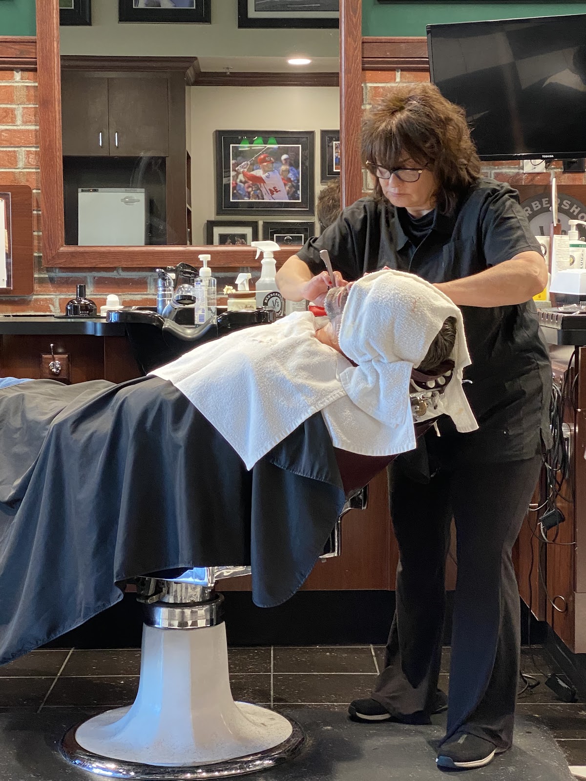 Barber applying hot towel shave service to reclined client